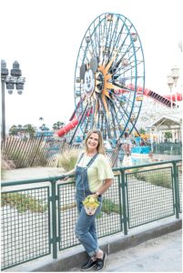 Woman standing at the rail in front of Mickey Mouse Ferris wheel. Photographer Donna Thompson wearing overalls and a Tinker Bell purse.