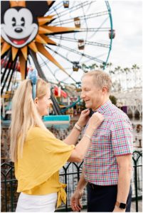 Woman straightening mans tie at Disneyland in front of the ferris wheel at Engagement Photography Session.