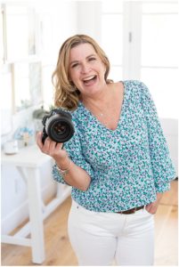 Woman laughing at the camera holding a canon camera wearing a blue floral blouse